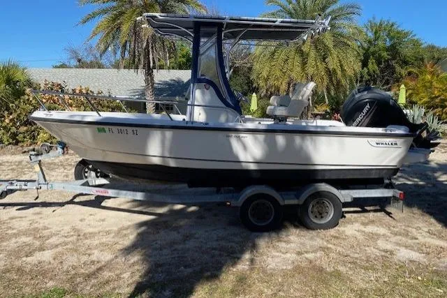 Slide: The Image of 2015 Boston Whaler 190 Outrage boat on trailer, parked outdoors with palm trees in background. - 5