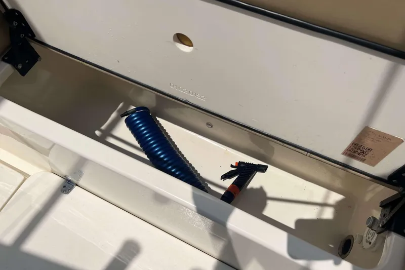 Slide: The Image of Storage compartment in 2021 Scout 305 LXF boat with blue hose and spray nozzle. - 8