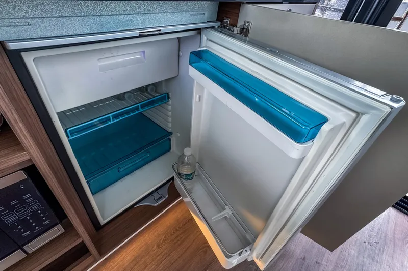 Slide: The Image of Compact refrigerator inside 2022 Beneteau Antares 11 Fly boat, featuring blue accents and wooden flooring. - 18