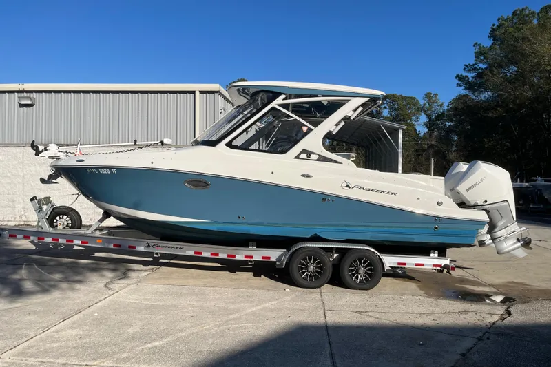 The Image of 2022 Finseeker 280 DC boat on trailer, blue and white design, parked outdoors. - 0