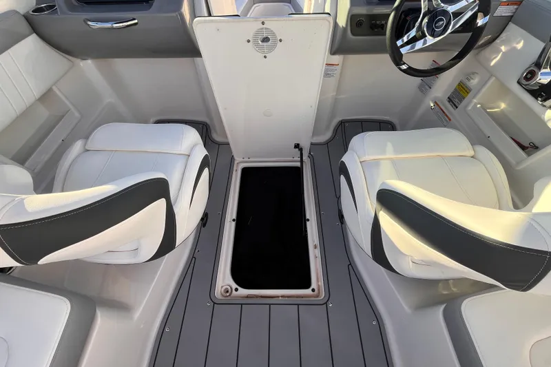 Slide: The Image of 2025 Chaparral 23 SSi OB boat interior with white and gray seating and open storage compartment. - 10