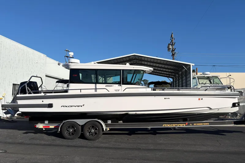 The Image of 2021 Axopar 28 Cabin boat on trailer, parked outdoors under clear blue sky. - 0