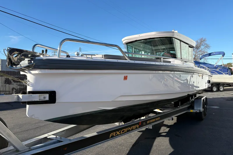 Slide: The Image of 2021 Axopar 28 Cabin boat on trailer, displayed outdoors under clear blue sky. - 2