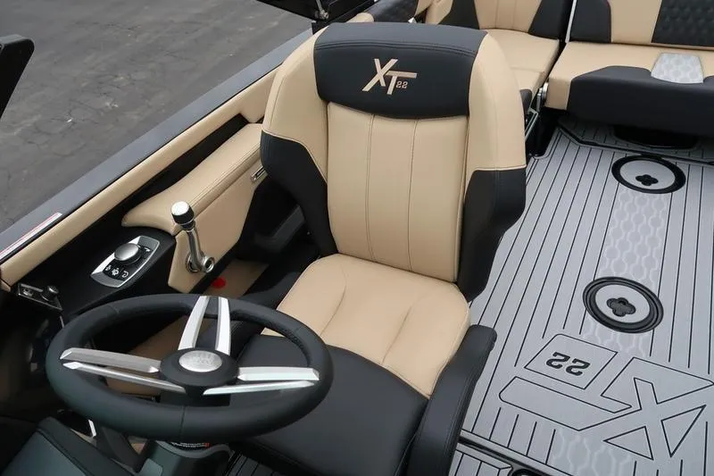 Slide: The Image of 2025 MasterCraft XT22 boat interior with beige and black seating, steering wheel, and floor design. - 49