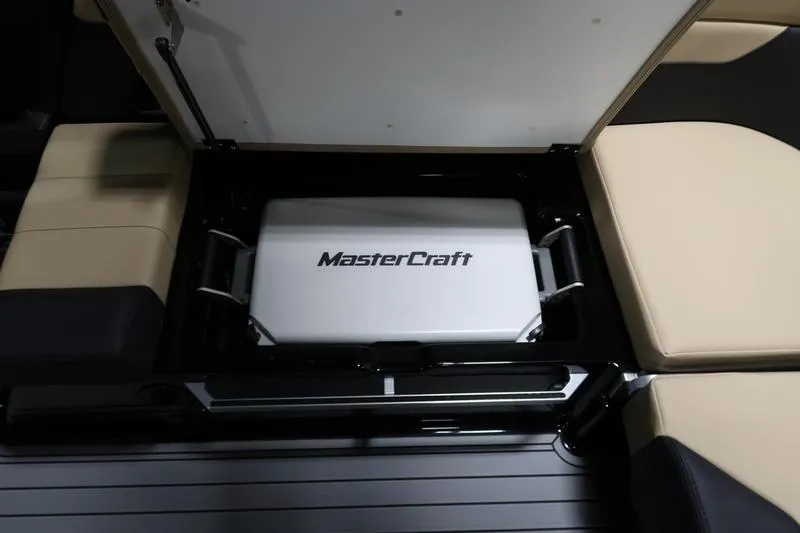 Slide: The Image of 2025 MasterCraft XT22 boat storage compartment with beige seating and branded cooler. - 58