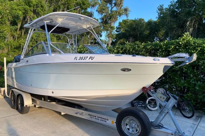 Slide: The Image of 2015 Robalo R247 Dual Console boat on trailer, surrounded by greenery. - 1
