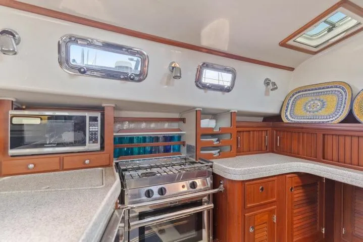 Slide: The Image of Galley kitchen in 2015 Blue Jacket 40 sailboat with stove, microwave, and wooden cabinetry. - 11