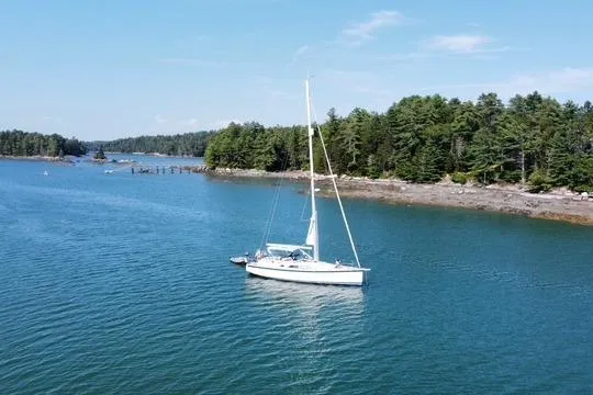 Slide: The Image of Sailboat Hallberg-Rassy 40C 2021 on serene blue water near forested shoreline. - 2