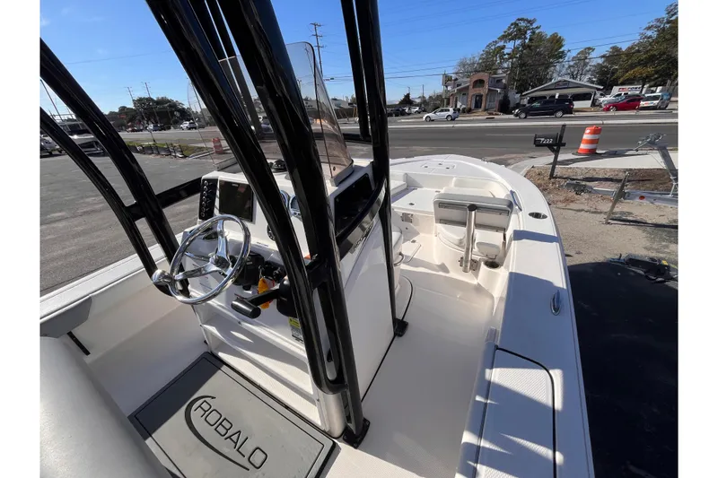 Slide: The Image of 2022 Robalo 226 Cayman boat interior with steering wheel and seating, parked near a road. - 9