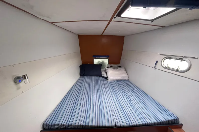 Slide: The Image of Cozy cabin interior of 2004 Lagoon 570 yacht with striped bedding and porthole window. - 49