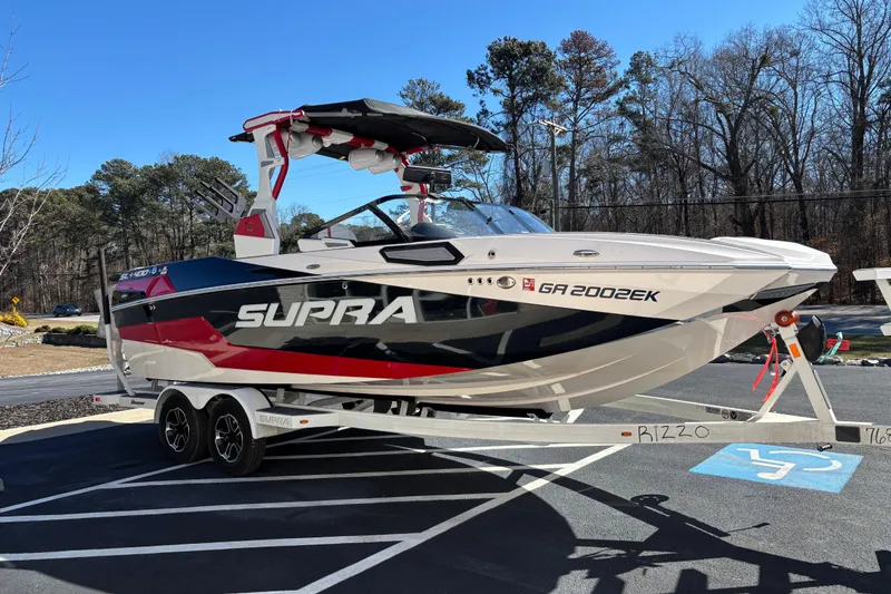 Slide: The Image of 2022 Supra SL 400 boat on trailer, parked outdoors, surrounded by trees. - 2