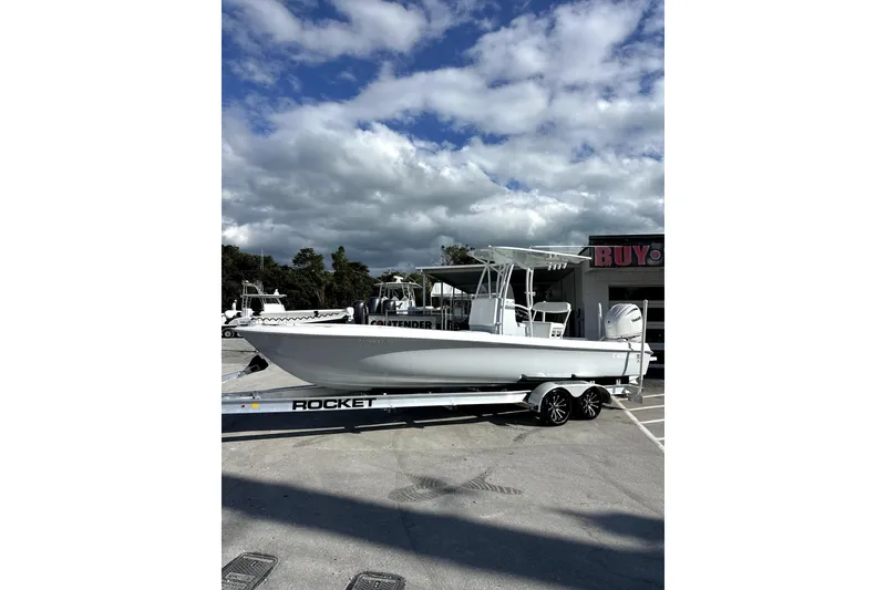 Slide: The Image of 2024 Contender 25 Bay boat on trailer, parked outdoors under clear blue sky. - 1