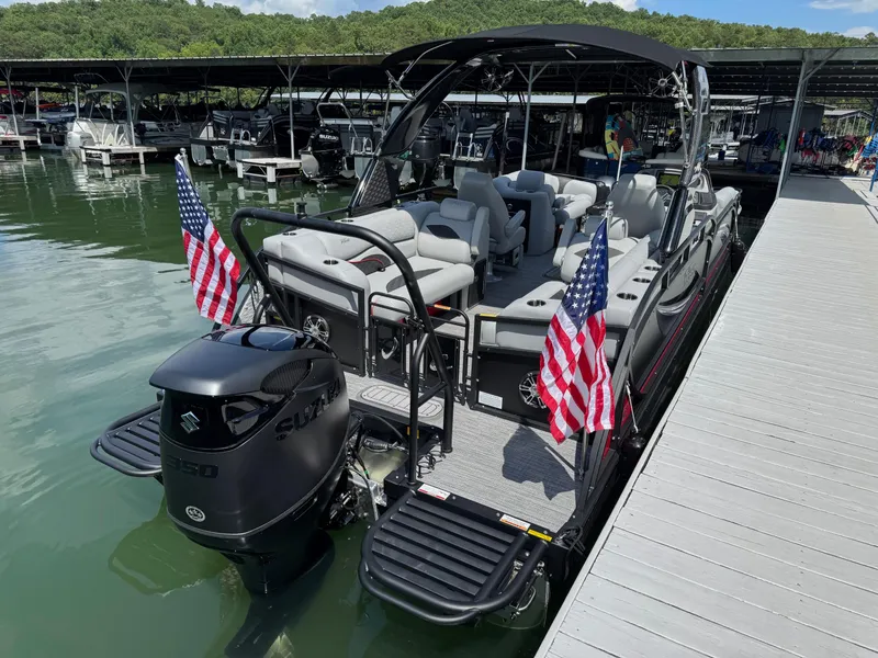 Slide: The Image of 2026 JC SportToon 24 TT DSL pontoon boat docked, featuring American flags and Suzuki outboard motor. - 22