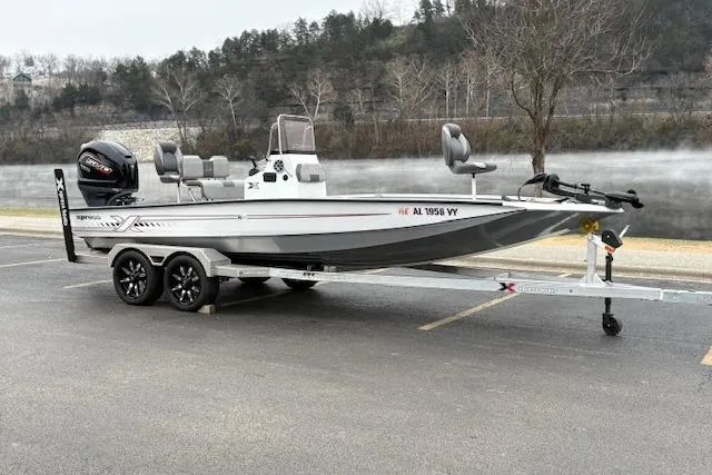 Slide: The Image of 2024 Express H22B boat on trailer, parked near a scenic lake with trees in the background. - 50