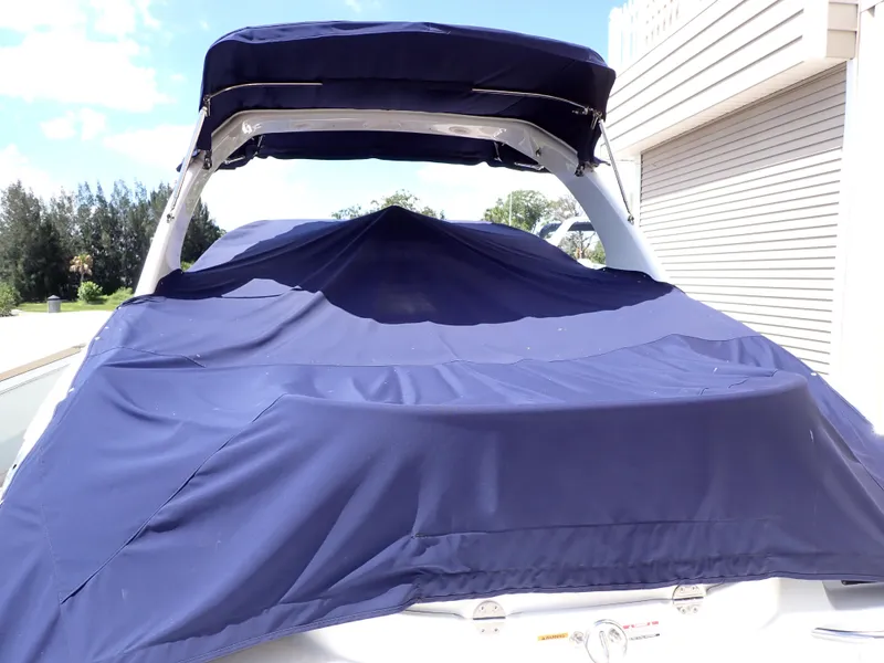 Slide: The Image of 2011 Chaparral 287 SSX boat with blue cover, parked near a building. - 3