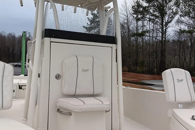 Slide: The Image of 2022 Ranger 2510 Bay boat interior with white seating and console, surrounded by trees. - 11