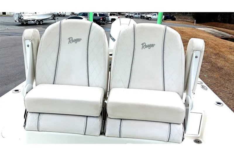Slide: The Image of 2022 Ranger 2510 Bay boat seats, white with diamond stitching, in a marina setting. - 16