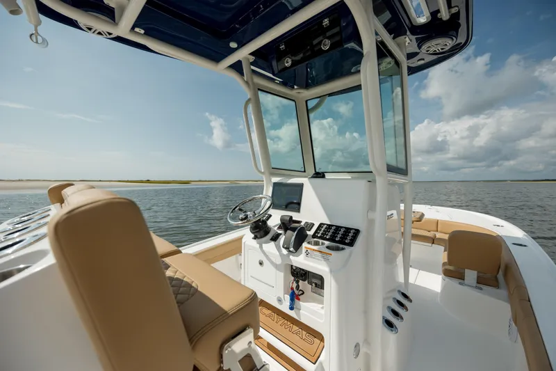 Slide: The Image of 2025 Caymas 26 HB boat interior with steering console, beige seating, and ocean view. - 16