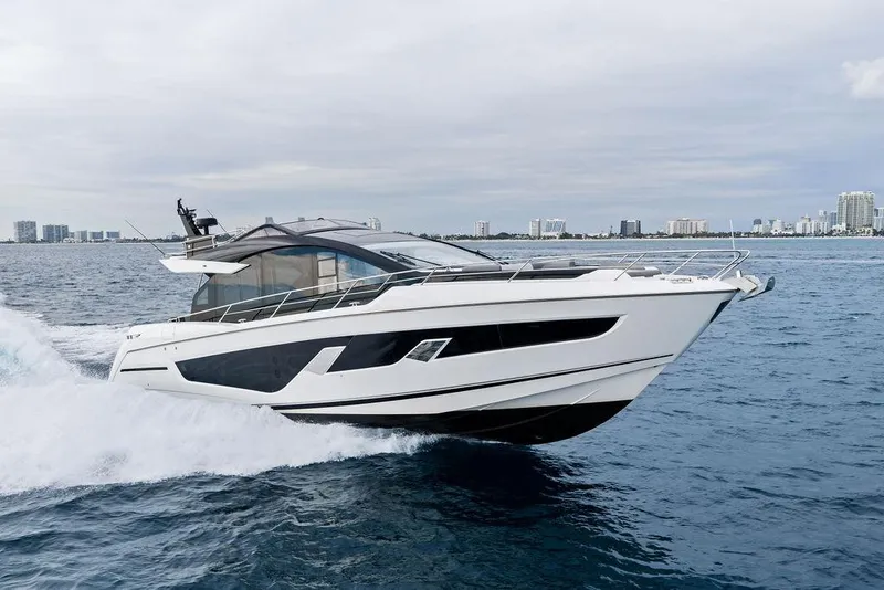 Slide: The Image of 2022 Sunseeker 65 Sport Yacht cruising on open water, city skyline in background. - 2