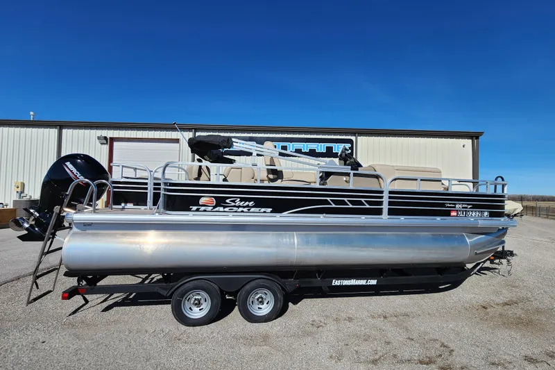 The Image of 2022 Sun Tracker Fishin' Barge 22 DLX pontoon boat on trailer, parked outdoors. - 1