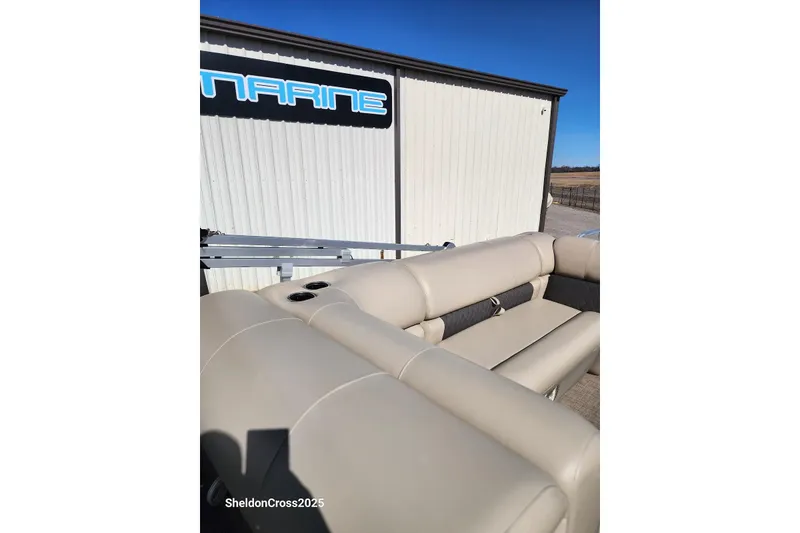 Slide: The Image of 2022 Sun Tracker Fishin' Barge 22 DLX with beige seating, parked near a marine building. - 8