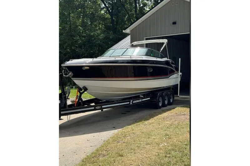 The Image of 2014 Formula 310 Bowrider on trailer outside a garage, surrounded by trees. - 1