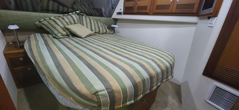 Slide: The Image of Cozy bedroom in 2004 Cabo 48 Convertible yacht with striped bedding and wooden cabinets. - 23