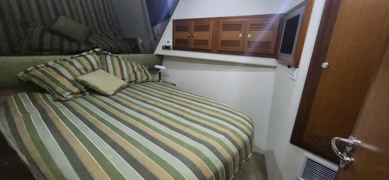 Slide: The Image of 2004 Cabo 48 Convertible cabin with striped bedding and wooden cabinetry. - 24