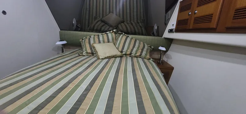 Slide: The Image of 2004 Cabo 48 Convertible cabin with striped bedding and wooden cabinets. - 25