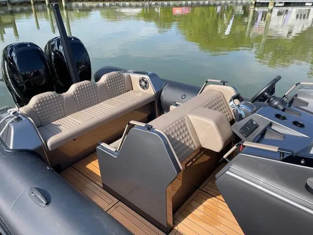Slide: The Image of 2022 Roughneck RIB 1010 boat interior with seating and controls, docked on calm water. - 6
