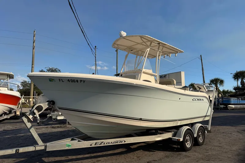 The Image of 2015 Cobia 201 Center Console boat on trailer, parked outdoors under clear sky. - 0