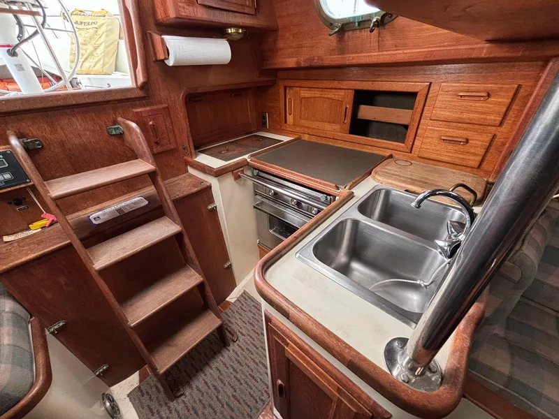 Slide: The Image of 1986 Pacific Seacraft 34 yacht interior with wooden cabinetry, compact kitchen, and stainless steel sink. - 11