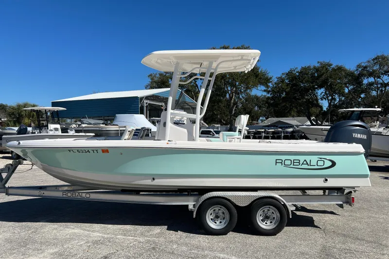 The Image of 2024 Robalo 226 Cayman boat on trailer, light blue hull, sunny day. - 0