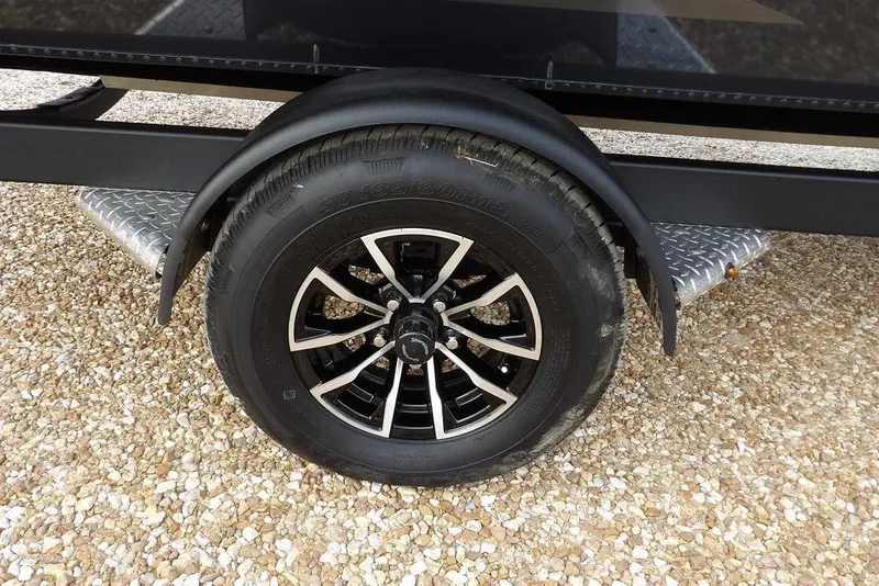 Slide: The Image of 2026 Lund 1875 Renegade trailer wheel on gravel, featuring black alloy rim. - 41