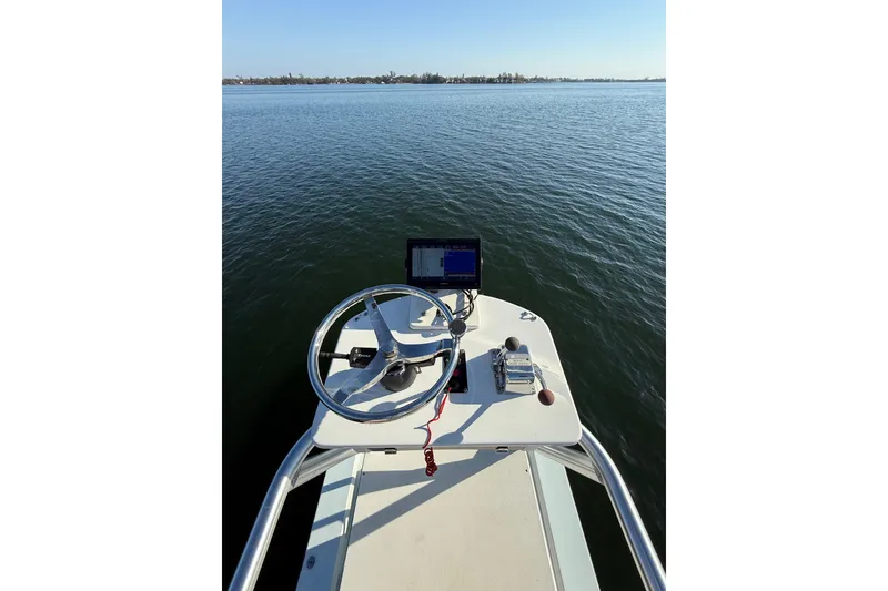 Slide: The Image of 1987 Privateer 22 Roamer boat helm with steering wheel and navigation equipment on calm water. - 24