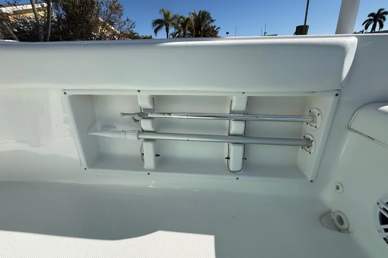 Slide: The Image of 2014 Sea Hunt Triton 220 boat storage compartment with rods, sunny day, palm trees in background. - 34