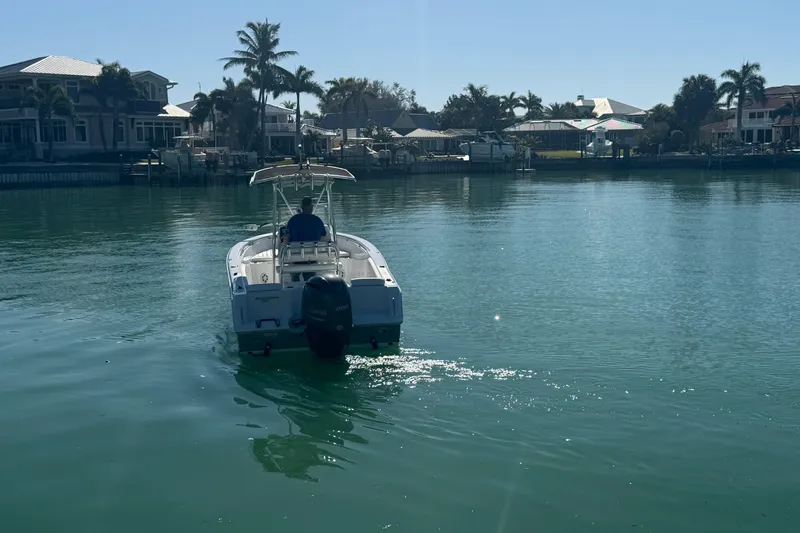 Slide: The Image of 2014 Sea Hunt Triton 220 boat cruising on a calm, sunny waterfront with palm trees. - 5