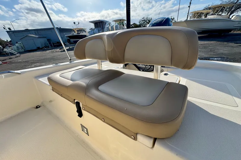 Slide: The Image of 2023 Scout 177 Sport boat with beige cushioned seating, docked under a partly cloudy sky. - 18