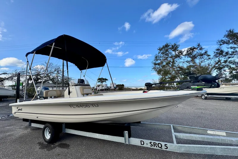 Slide: The Image of 2023 Scout 177 Sport boat on trailer with canopy, parked outdoors under blue sky. - 2
