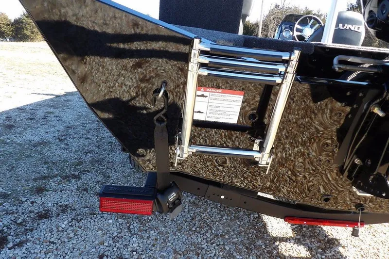 Slide: The Image of 2026 Lund 1875 Renegade boat with ladder and warning label, parked on gravel. - 46