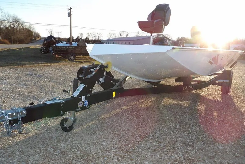 Slide: The Image of 2026 Lund 1875 Renegade boat on trailer, sunlit background, gravel surface. - 39