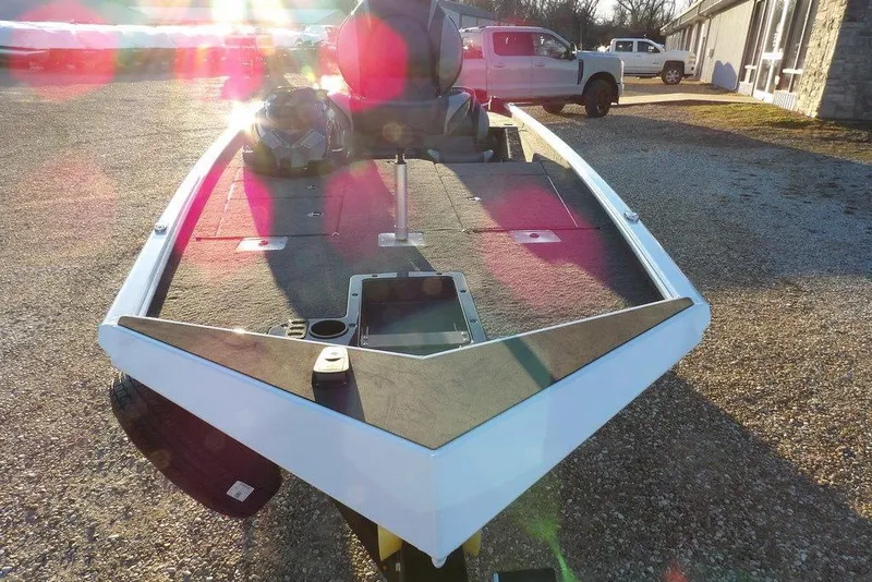 Slide: The Image of 2026 Lund 1875 Renegade boat on gravel, sunlit, with vehicles in background. - 7