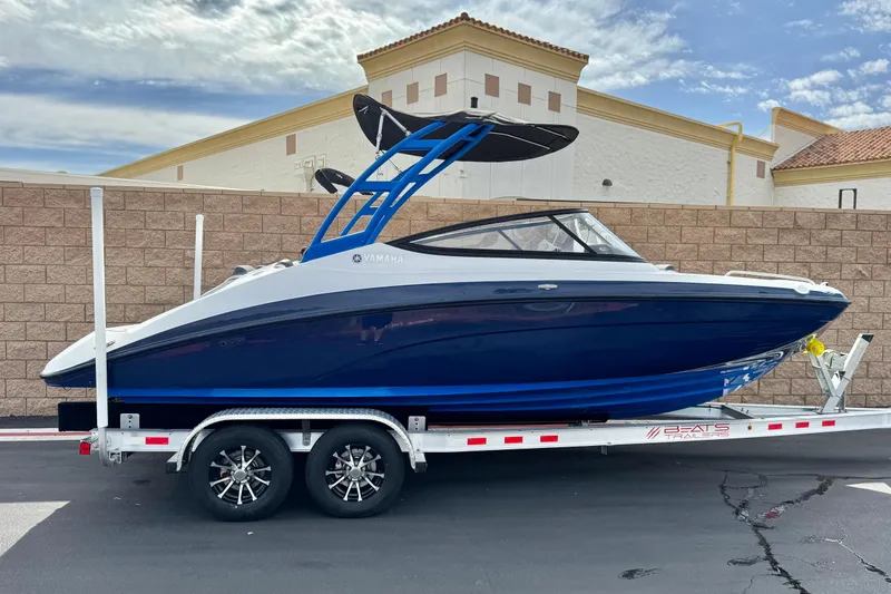 The Image of 2020 Yamaha AR210 boat on trailer, blue and white design, parked outdoors. - 0