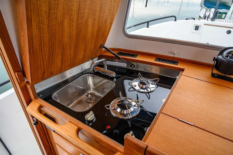 Slide: The Image of 2024 Targa 27.2 boat kitchen with stove and sink, featuring wooden cabinetry. - 47