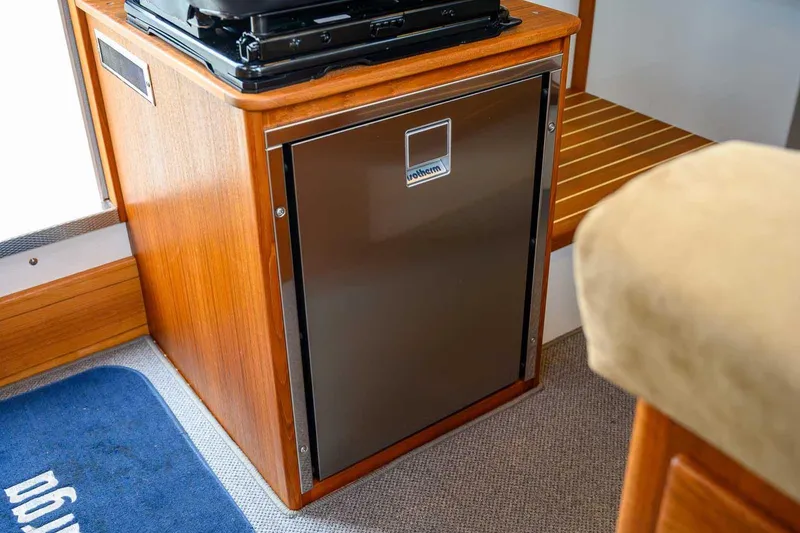 Slide: The Image of 2024 Targa 27.2 interior with compact fridge and wooden cabinetry. - 48