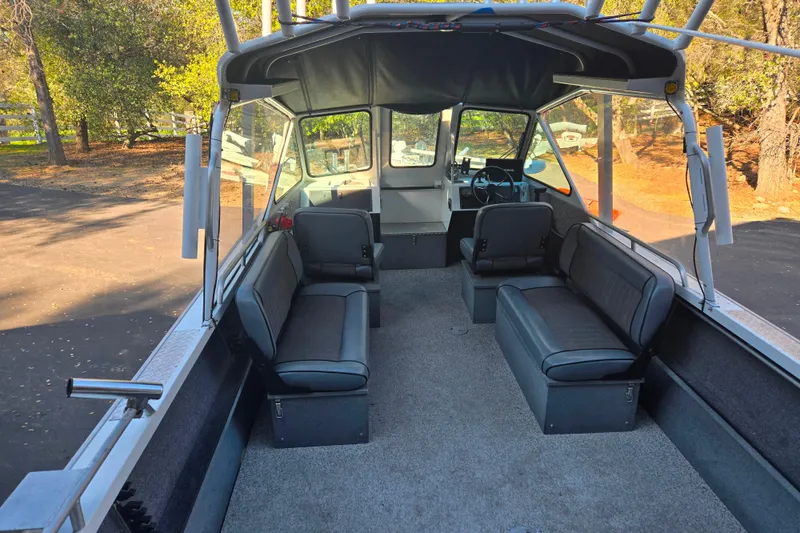 Slide: The Image of 2021 Alumaweld Intruder Outboard 20 interior with seating and steering wheel, parked outdoors. - 7