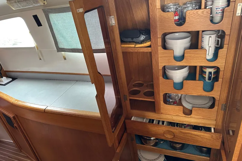 Slide: The Image of Interior of 2008 Seawind 1000 XL showing organized wooden kitchen storage with dishes and cups. - 11