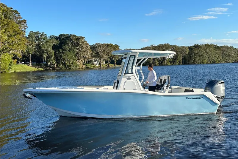 Slide: The Image of 2023 Tidewater 232 LXF boat cruising on a scenic lake with lush greenery. - 5