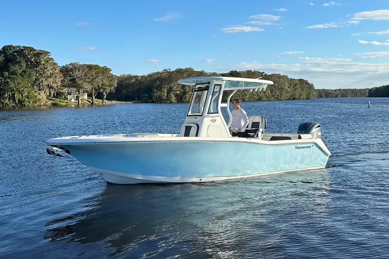Slide: The Image of 2023 Tidewater 232 LXF boat cruising on a serene lake under a clear blue sky. - 6
