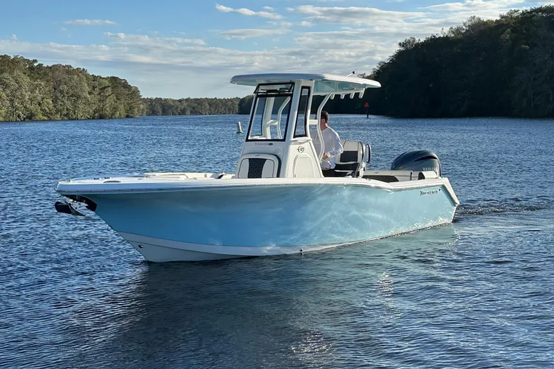 Slide: The Image of 2023 Tidewater 232 LXF boat cruising on a serene lake with lush forest backdrop. - 7